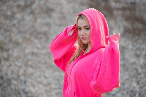 Portret van een modieus blond meisje in een ping gekleurde hoodie - Foto, afbeelding