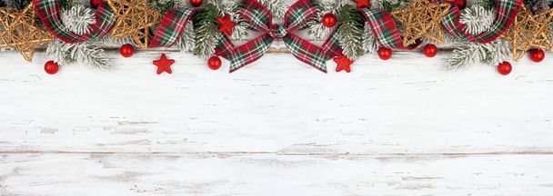 Christmas top border of ornaments, branches and red and green plaid bows and ribbon. Overhead view on a white wood background. Copy space. - Photo, Image