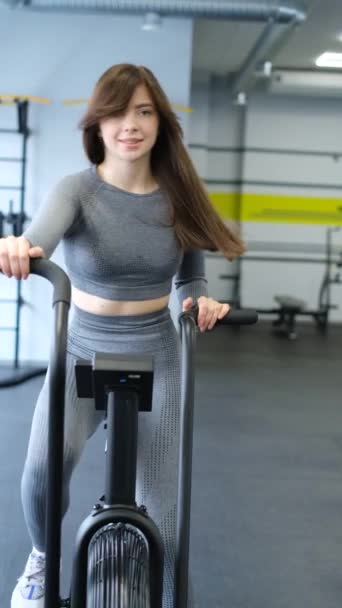 Přizpůsobit atraktivní brunetka mladá žena dělá cvičení na kole v tělocvičně. Mladá sportovní žena dělá kardiochirurgický trénink. Fitness, CrossFit a koncepce cvičení. Svislé video. - Záběry, video