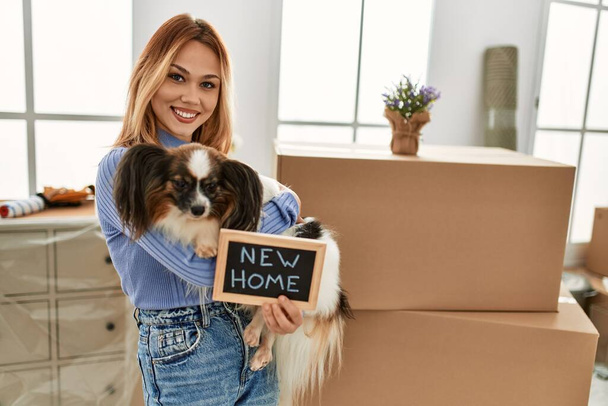 Young caucasian woman holding blackboard hugging dog at new home - Valokuva, kuva