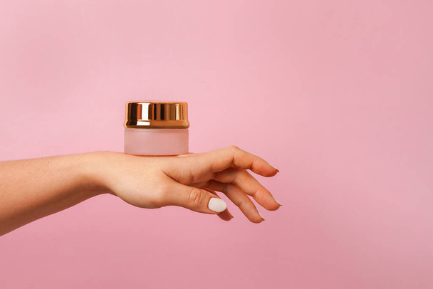 Frasco de ouro de creme cosmético na mão feminina, fundo rosa. Cosmético produto de beleza marca mockup. Espaço de cópia - Foto, Imagem