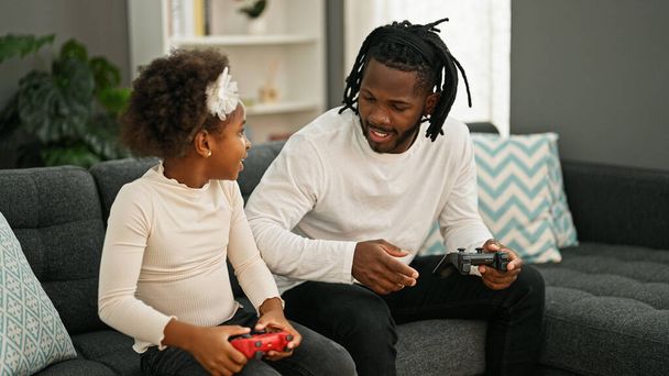 Αφρο-αμερικανός πατέρας και η κόρη παίζουν βιντεοπαιχνίδι κάθεται στον καναπέ στο σπίτι - Φωτογραφία, εικόνα