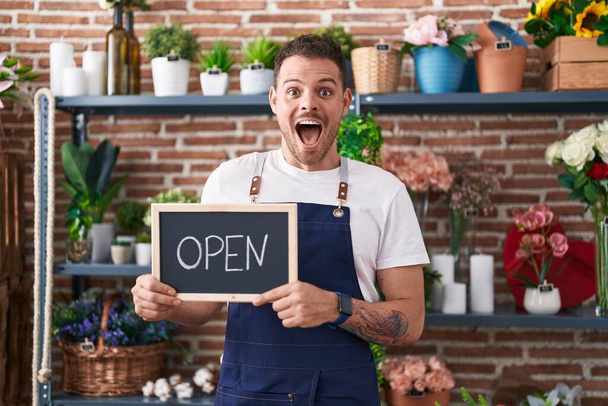 Young hispanic man working at florist holding open sign celebrating crazy and amazed for success with open eyes screaming excited.  - Photo, Image