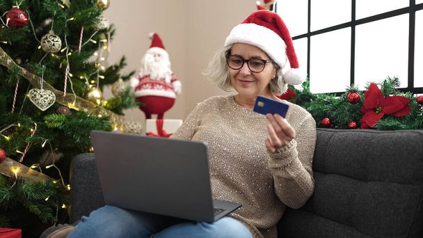Frau mittleren Alters mit grauen Haaren beim Online-Weihnachtseinkauf mit Laptop zu Hause - Foto, Bild