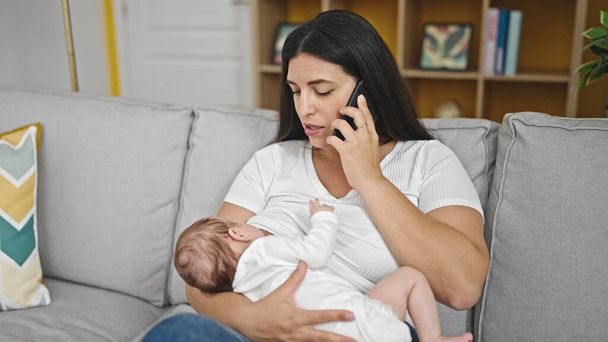 Мати і дитина дочка сидять на дивані грудного вигодовування, розмовляючи по телефону вдома - Фото, зображення