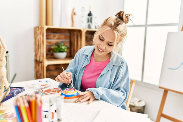 Jonge blanke vrouw kunstenaar glimlachen zelfverzekerd tekenen keramiek in kunststudio - Foto, afbeelding
