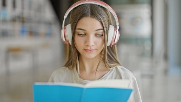 Joven chica hermosa estudiante leyendo libro escuchando música en la biblioteca - Foto, Imagen
