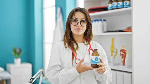 Fiatal gyönyörű spanyol nő orvos bemutató gyógyszeres üveg a klinikán - Fotó, kép