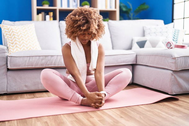 Afro-Amerikaanse vrouw stretching benen zitten op de vloer thuis - Foto, afbeelding