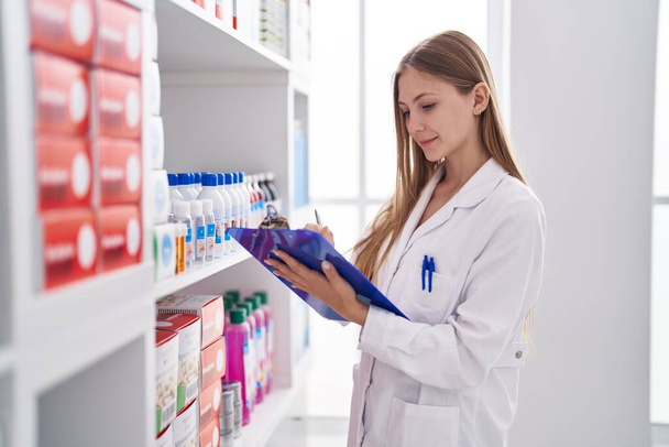Young caucasian woman pharmacist writing on document at pharmacy - Photo, Image