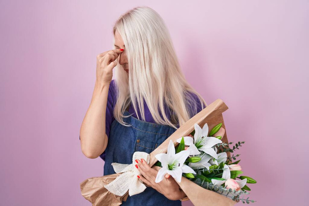 Femme caucasienne tenant un bouquet de fleurs blanches fatigué se frottant le nez et les yeux ressentant fatigue et maux de tête. concept de stress et de frustration.  - Photo, image