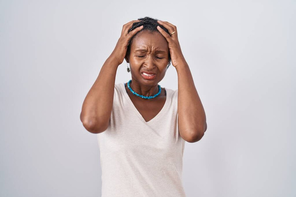 Mulher africana com dreadlocks em pé sobre fundo branco sofrendo de dor de cabeça desesperada e estressada porque dor e enxaqueca. mãos na cabeça.  - Foto, Imagem