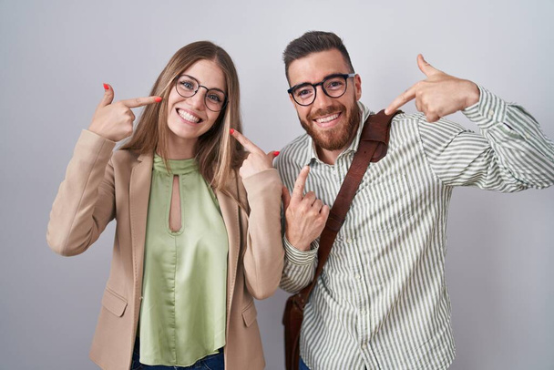Mladý pár stojí nad bílým pozadím a vesele se usmívá, ukazuje a ukazuje prsty a ústy. koncepce stomatologického zdraví.  - Fotografie, Obrázek
