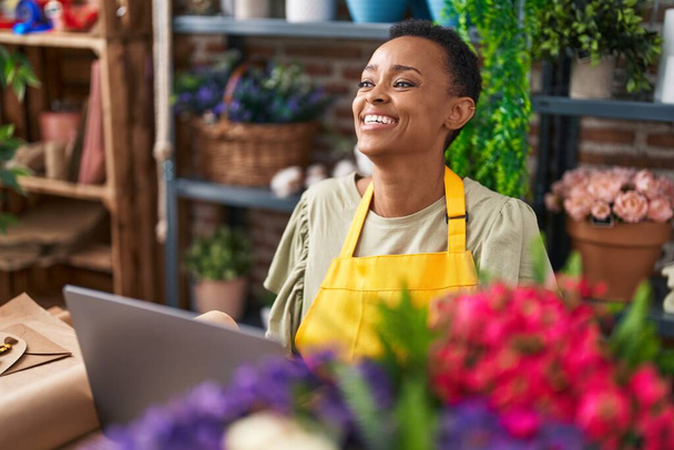 Afrykańska amerykanka kwiaciarnia uśmiechnięta pewnie przy użyciu laptopa w kwiaciarnia - Zdjęcie, obraz