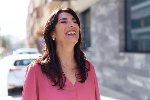 Middle age hispanic woman smiling confident looking to the side at street - Photo, image