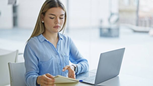 Młoda blondynka biznes pracownik za pomocą laptopa czytania notebooka w biurze - Zdjęcie, obraz