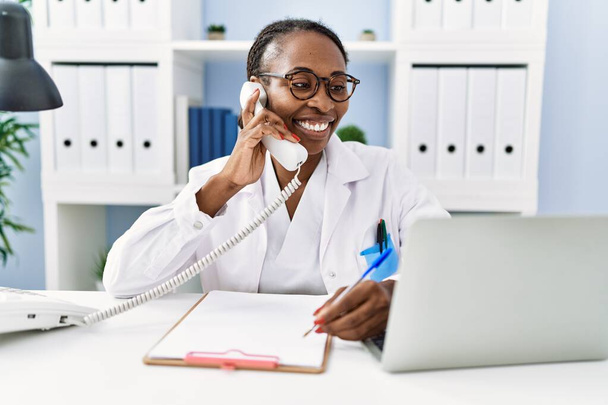 Medico afroamericano donna che parla al telefono scrivendo su documento in clinica - Foto, immagini