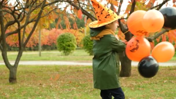 Menino comemorando Halloween, girando alegremente no parque segurando um monte de balões em suas mãos. - Filmagem, Vídeo