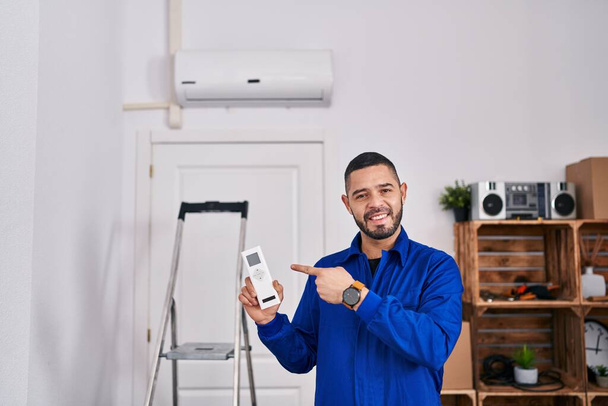 Hispanische Reparaturfirma, die mit Klimaanlage arbeitet, lächelt glücklich und zeigt mit Hand und Finger  - Foto, Bild