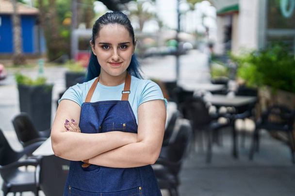Young caucasian woman waitress smiling confident standing with arms crossed gesture at coffee shop terrace - 写真・画像