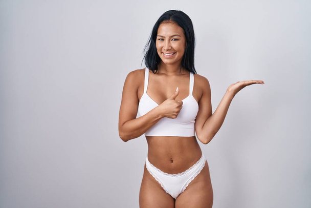 Femme hispanique portant de la lingerie montrant la main de la paume et faisant un geste correct avec les pouces levés, souriant heureux et joyeux  - Photo, image