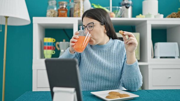 Young hispanic woman using tablet having breakfast at dinning room - Photo, Image