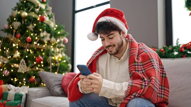 Jovem hispânico celebrando o Natal usando smartphone em casa - Foto, Imagem