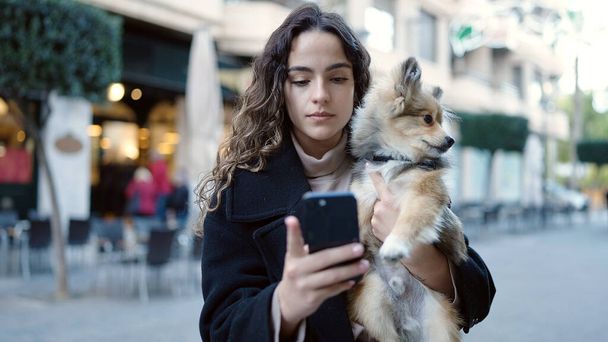 Mladá hispánská žena se psem pomocí smartphonu na ulici - Fotografie, Obrázek