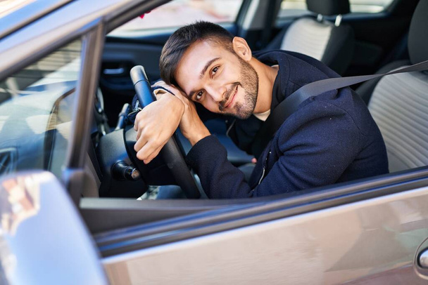 Jeune homme hispanique souriant confiant appuyé sur le volant dans la rue - Photo, image