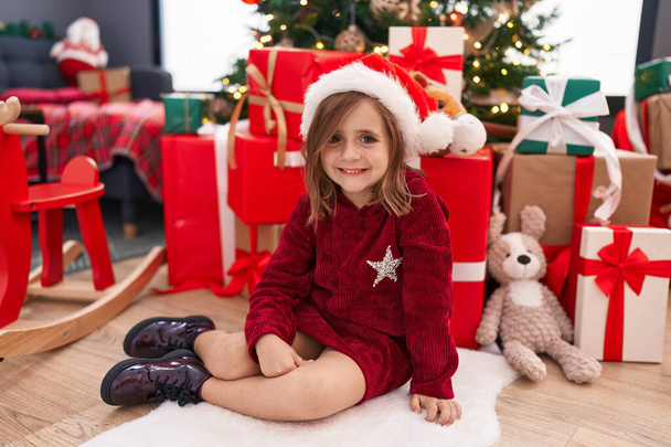 Rozkošný hispánský dívka usměvavý jistý sedí na podlaze u vánočního stromečku doma - Fotografie, Obrázek