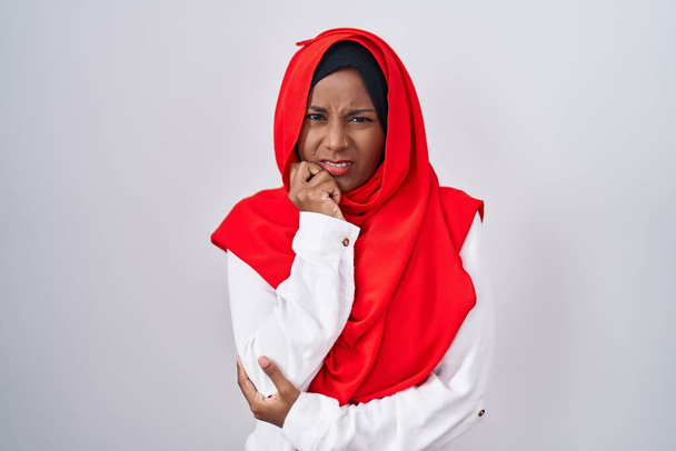 Jonge Arabische vrouw draagt traditionele islamitische hijab sjaal kijken gestresst en nerveus met handen op de mond bijtende nagels. angstprobleem.  - Foto, afbeelding