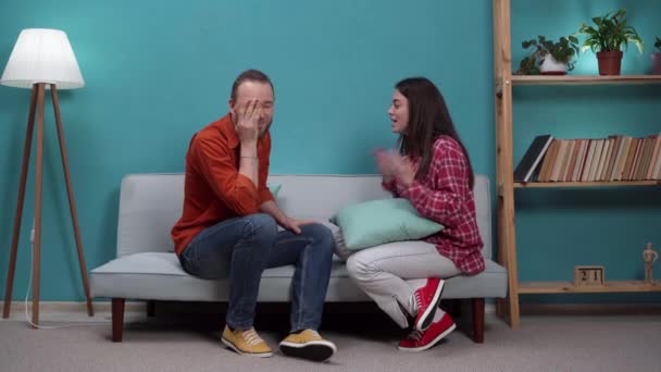 Frustrierte junge Paare sitzen auf der Couch und streiten sich, Frau schlägt Mann mit Kopfkissen. Kopierraum - Filmmaterial, Video