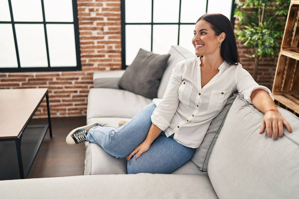Νέα όμορφη ισπανόφωνη γυναίκα χαμογελά αυτοπεποίθηση κάθεται στον καναπέ στο σπίτι - Φωτογραφία, εικόνα
