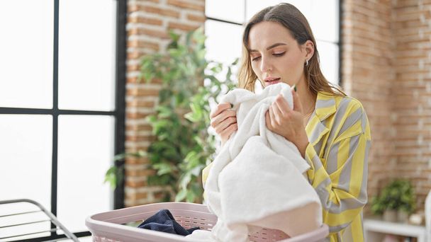 Νεαρή ξανθιά γυναίκα μυρίζει καθαρές πετσέτες στο πλυσταριό - Φωτογραφία, εικόνα