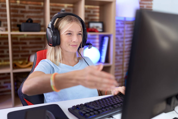 Nuori valkoihoinen nainen pelaa videopelejä yllään kuulokkeet hymyilevä ystävällinen tarjoaa kädenpuristus tervehdys ja kutsuva. menestyksekäs liiketoiminta.  - Valokuva, kuva