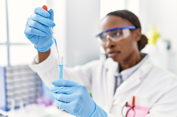Afrikaans amerikaanse vrouw wetenschapper gieten vloeistof op reageerbuis in laboratorium - Foto, afbeelding