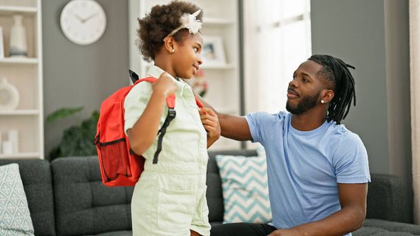 アフリカ系アメリカ人の父親と娘は,自宅で学校に行く準備をしているバックパックを着ています. - 写真・画像