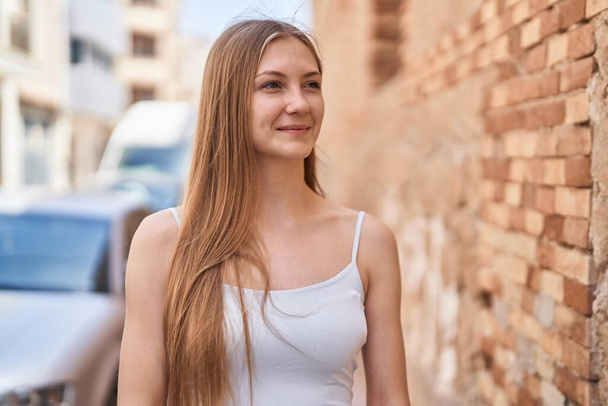 Молодая белая женщина, уверенно улыбающаяся, глядя в сторону улицы - Фото, изображение