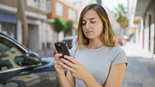 Havalı, genç, sarışın bir kadın, şehir sokağının dışında akıllı telefonuna dalmış. Çevrimiçi yaşam tarzına kendini kaptırmış beyaz kadın mesajlaşması.. - Fotoğraf, Görsel