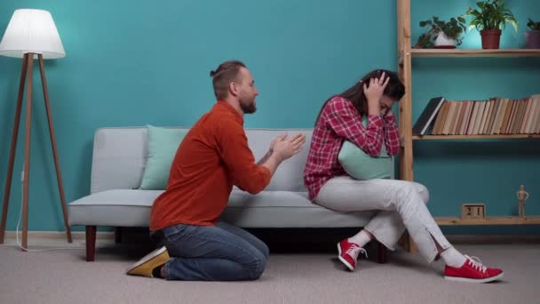Casamento casal depois de uma briga no sofá. Marido pede perdão à esposa de joelhos na sala de estar. Espaço de cópia - Filmagem, Vídeo