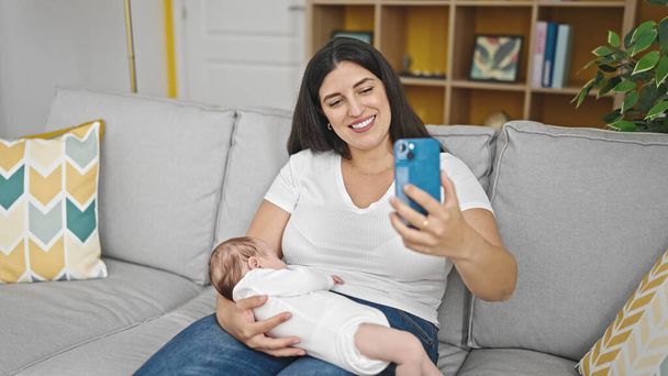 Mother and baby daughter sitting on sofa taking selfie picture at home - Photo, Image