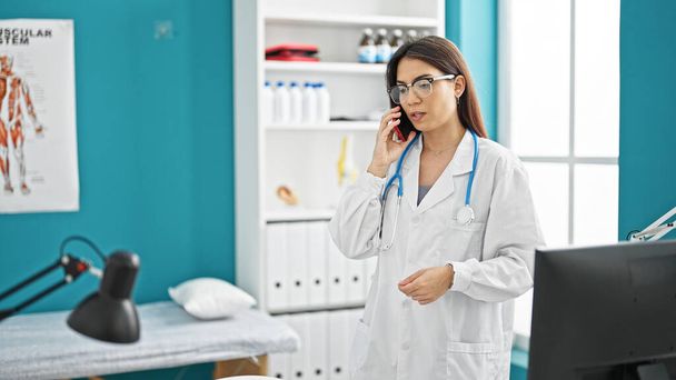 Joven hermosa mujer hispana médico hablando en teléfono inteligente sonriendo en la clínica - Foto, imagen