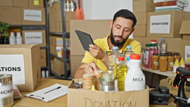 Junger hispanischer Mann hilft im Charity Center mit Touchpad bei der Überprüfung von Produkten - Foto, Bild