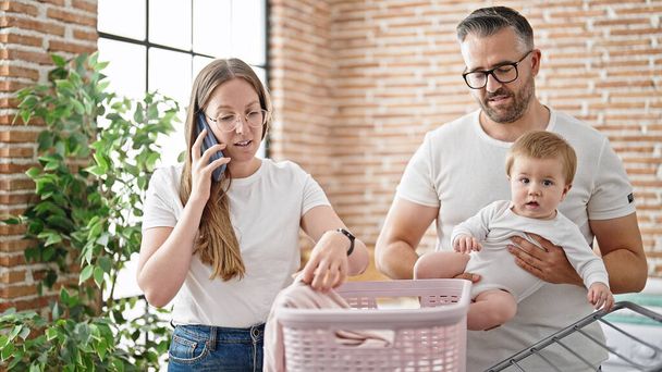 Famiglia di madre, padre e bambino che fanno il bucato parlando al telefono in lavanderia - Foto, immagini
