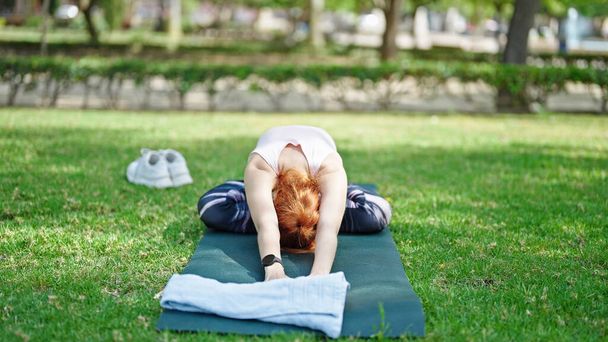 Młoda ruda kobieta trening jogi ćwiczenia siedzi na zioło w parku - Zdjęcie, obraz