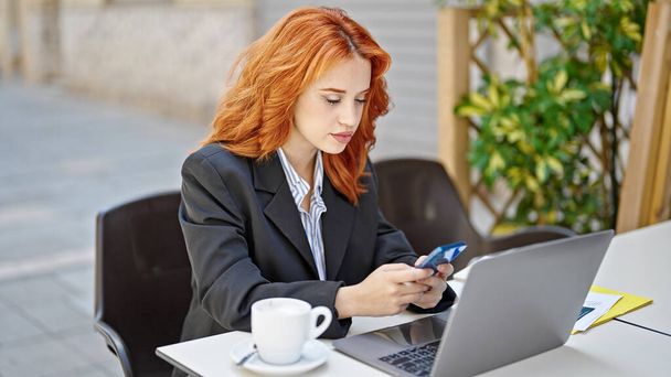 Nuori punapää nainen liiketoiminnan työntekijä, joka käyttää älypuhelinta kahvilan terassilla - Valokuva, kuva