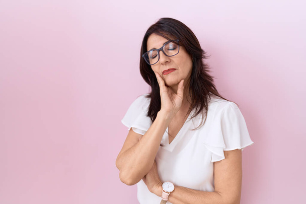 Středního věku hispánská žena na sobě ležérní bílé tričko a brýle myšlení vypadat unaveně a znuděný deprese problémy se zkříženými pažemi.  - Fotografie, Obrázek