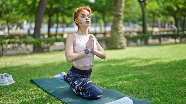 Genç kızıl saçlı kadın yoga egzersizi yapıyor parkta otun üzerinde oturuyor. - Fotoğraf, Görsel