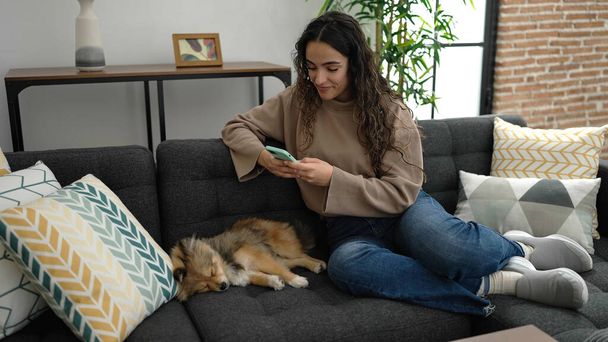Mladá hispánská žena se psem fotit smartphone na spícího psa doma - Fotografie, Obrázek