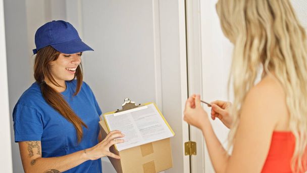 Young beautiful hispanic woman delivery woman giving package to client signing document at home - Foto, Bild